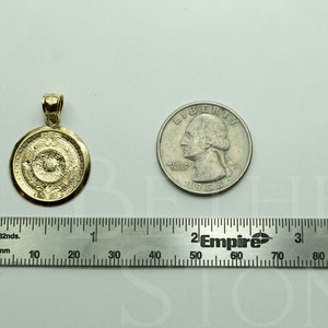May include: A gold-coloured pendant in the shape of a round medallion with intricate designs. The pendant is about the size of a UK 20 pence coin.