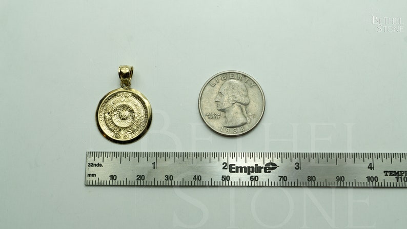 May include: A gold-coloured pendant in the shape of a round medallion with intricate designs. The pendant is about the size of a UK 20 pence coin.