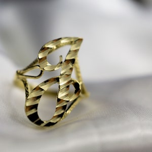 May include: A gold ring featuring a diamond-cut design in the shape of the letter "B".