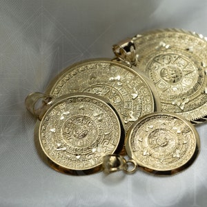 May include: Four gold-toned pendants featuring the Aztec calendar, also known as the Sun Stone, in different sizes. The pendants are intricately detailed and have a textured surface.