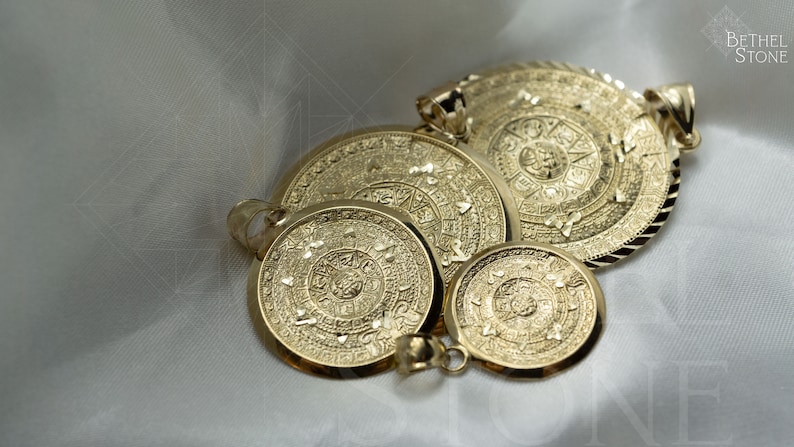May include: Four gold-toned pendants featuring the Aztec calendar, also known as the Sun Stone, in different sizes. The pendants are intricately detailed and have a textured surface.