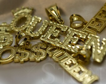May include: A close-up of a group of gold-plated pendants, including the words "QUEEN" and "BOSS". The pendants are intricately designed with a diamond-cut pattern.