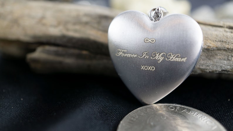 Op de afbeelding: Een zilveren hartvormig medaillon met een oneindigheidssymbool en de inscriptie "Forever In My Heart XOXO".