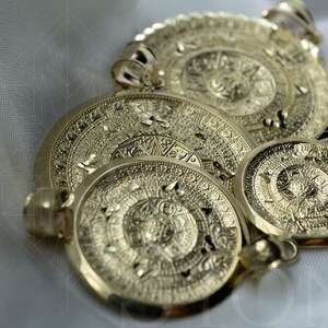 May include: Three gold-toned Aztec calendar pendants of varying sizes. The pendants are intricately detailed with circular patterns and symbols.