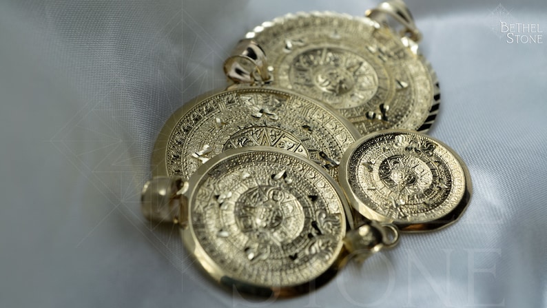 May include: Three gold-toned Aztec calendar pendants of varying sizes. The pendants are intricately detailed with circular patterns and symbols.