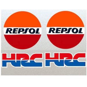 Könnte beinhalten: Zwei rote, weiße und orangefarbene runde Aufkleber mit dem Wort "REPSOL" in schwarzer Schrift. Unter den Aufklebern befinden sich zwei rote, weiße und blaue Aufkleber mit dem Text "HRC" in weißer Schrift.