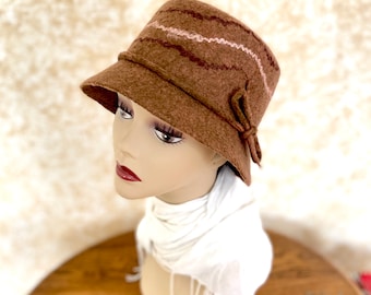 May include: A brown felt hat with pink and brown wavy lines. The hat has a wide brim and a bow on the side.