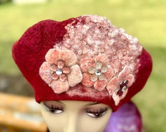 May include: A red felt beret with three decorative flower appliqués. The flowers are in shades of pink and peach, with sparkling rhinestone centers. The beret has a textured, light pink section on top.
