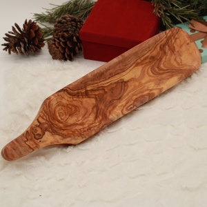 Könnte beinhalten: Ein langes, hölzernes Serviertablett mit einem natürlichen Holzmaserungsmuster. Das Tablett hat an einem Ende einen Griff und ist aus Olivenholz gefertigt.