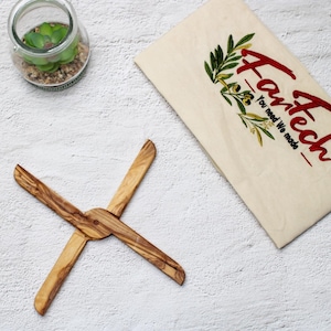 Peut inclure: Un ustensile de cuisine en bois en forme de croix. L'ustensile est en bois d'olivier et a une finition naturelle. L'ustensile est sur une surface blanche.