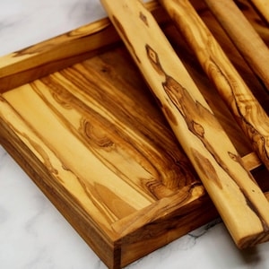 Puede incluir: Una bandeja de servir de madera con un acabado de madera natural y un dise&ntilde;o de listones. La bandeja est&aacute; hecha de madera de olivo y tiene una forma rectangular.