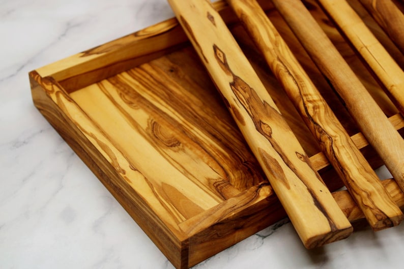 Puede incluir: Una bandeja de servir de madera con un acabado de madera natural y un dise&ntilde;o de listones. La bandeja est&aacute; hecha de madera de olivo y tiene una forma rectangular.
