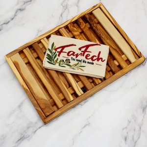 Puede incluir: Una bandeja de servir de madera con un acabado natural y un diseño tejido. La bandeja está hecha de madera de olivo y tiene una forma rectangular. Una servilleta de tela blanca con el texto "FanTech - You need We made" está colocada en la bandeja.