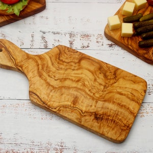May include: A large, rectangular olive wood cutting board with a handle. The board has a natural wood grain pattern and is perfect for serving cheese, crackers, and other appetizers.