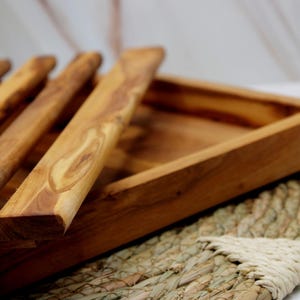 Puede incluir: Una bandeja de servir de madera con un acabado de madera natural y un juego de utensilios de servir de madera. La bandeja es rectangular y tiene un borde elevado. Los utensilios est&aacute;n hechos del mismo tipo de madera y tienen un acabado liso.