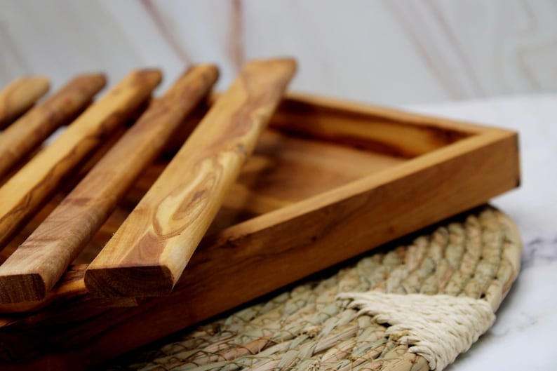 Puede incluir: Una bandeja de servir de madera con un acabado de madera natural y un juego de utensilios de servir de madera. La bandeja es rectangular y tiene un borde elevado. Los utensilios est&aacute;n hechos del mismo tipo de madera y tienen un acabado liso.