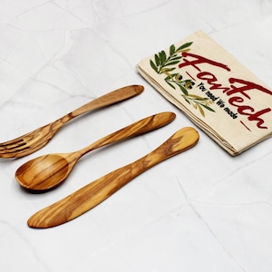 Könnte beinhalten: Ein Set aus drei Küchenutensilien aus Holz: eine Gabel, ein Löffel und ein Buttermesser. Die Utensilien sind aus Olivenholz gefertigt und haben eine natürliche Oberfläche. Die Utensilien sind auf einer weißen Oberfläche mit einem weißen Tuch angeordnet, auf dem der Text "Fartech - You need it, We made it" aufgedruckt ist.