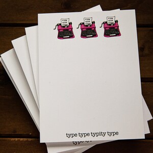 May include: A stack of white notepads with a pink typewriter illustration and the text "type type typity type" at the bottom.