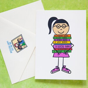Peut inclure: Une carte de vœux avec une illustration de dessin animé d'une personne tenant une pile de livres. Les livres sont étiquetés avec différents types de livres, tels que "un livre amusant", "un livre effrayant", "un livre d'histoire", "un livre triste", "un bon livre", "un mystère" et "un livre intelligent".
