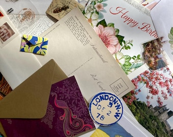 May include: A pile of colorful postcards and envelopes with various designs, including a peacock, a hibiscus flower, and a hand with a red outline. The text "Happy Birthday" is visible on one of the cards. The text "LONDON. N.W. DE 2 78" is visible on a blue and white circular sticker.