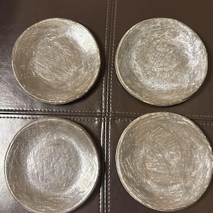 May include: Four round, gray ceramic plates with a white glaze. The plates have a textured surface and are arranged in a square pattern.