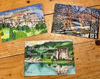 May include: Three Christmas cards featuring snowy winter scenes from Scotland. The first card shows Edinburgh Castle with the text "Merry Christmas from Edinburgh". The second card shows the Forth Rail Bridge with the text "Merry Christmas from Scotland". The third card shows a castle with a bridge and the text "Merry Christmas from Scotland".