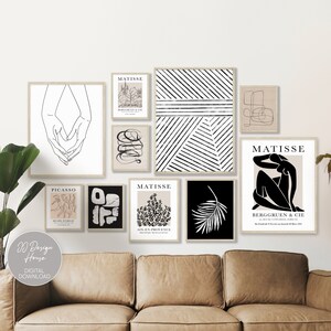 Puede incluir: Una pared de galería con impresiones de arte abstracto en blanco y negro, que incluyen un dibujo lineal de manos, una hoja de palma y un patrón geométrico. Las impresiones están dispuestas en una pared blanca sobre un sofá de cuero marrón.
