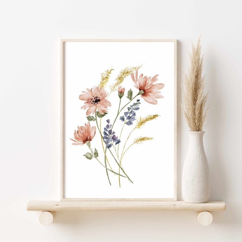 May include: Watercolor floral art print featuring a bouquet of pink and purple flowers with green leaves and yellow accents. The artwork is framed in a light wood frame and displayed on a wooden shelf. A white vase with dried grass is to the right.