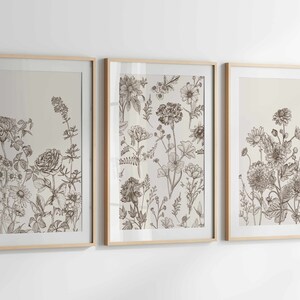 May include: Three framed botanical art prints. Each print features detailed line drawings of various flowers and foliage in shades of brown and beige. The frames are light wood.
