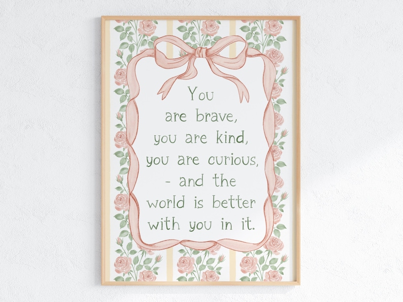 May include: A framed print with a light wood frame. The artwork features a pink ribbon and floral border, with the words "You are brave, you are kind, you are curious, - and the world is better with you in it." in the center.