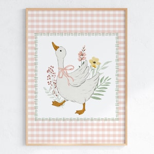 May include: A framed print featuring a watercolor illustration of a white goose with a pink bow around its neck, surrounded by flowers and greenery. The background has a pink and white gingham pattern, framed by a decorative border.