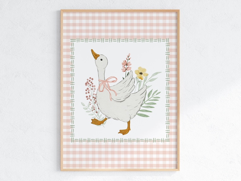 May include: A framed print featuring a watercolor illustration of a white goose with a pink bow around its neck, surrounded by flowers and greenery. The background has a pink and white gingham pattern, framed by a decorative border.