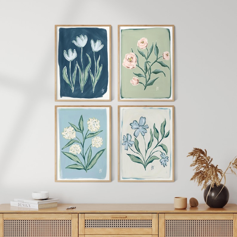 May include: Four framed floral art prints. Each print features a different floral arrangement in soft colors: white tulips on navy, pink roses on sage green, white hydrangeas on light blue, and blue flowers on cream. The frames are a light wood color.