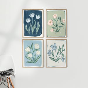 May include: Four framed floral art prints. Each print features a different flower design in a soft color palette. The top left print has white tulips on a navy background. The top right print has pink flowers on a green background.