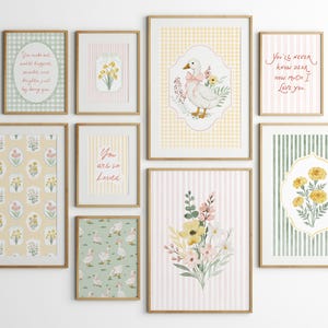 May include: A collection of framed art prints with a soft, pastel color palette. The prints feature floral patterns, a goose illustration, and inspirational quotes. The frames are a light wood color, and the overall aesthetic is charming and whimsical.