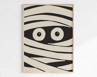 May include: A framed print featuring a mummy design. The artwork depicts a mummy's face with large, round eyes peeking through beige bandages. The background is black, and the frame is a light wood color. A Halloween-themed decorative item.