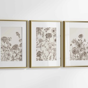 May include: Three framed botanical art prints. Each print features detailed sepia-toned illustrations of various flowers and foliage. The frames are gold-colored, adding a touch of elegance to the floral artwork. The prints are displayed against a white background.
