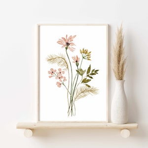 May include: Watercolor floral art print featuring a bouquet of pink and yellow flowers with green leaves and brown accents. The artwork is framed in a light wood frame and displayed on a wooden shelf. A white vase with dried grass is to the right.