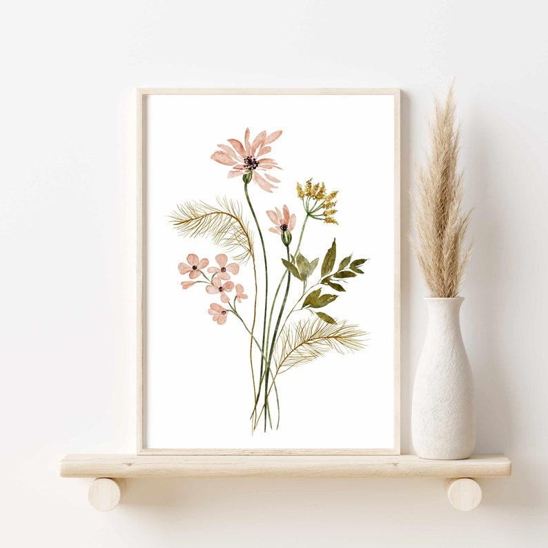 May include: Watercolor floral art print featuring a bouquet of pink and yellow flowers with green leaves and brown accents. The artwork is framed in a light wood frame and displayed on a wooden shelf. A white vase with dried grass is to the right.