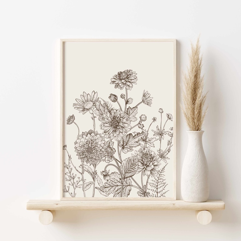 May include: A framed botanical print featuring a detailed pen and ink illustration of various flowers and foliage. The artwork is in shades of brown and cream, with a minimalist aesthetic. A white vase with dried pampas grass sits on a wooden shelf.