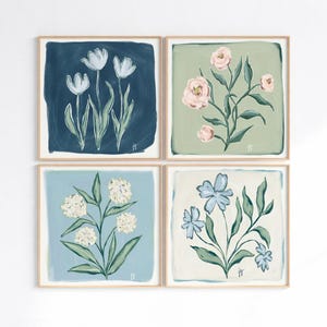 May include: Four framed floral art prints. Each square print features a different flower design: white tulips on navy, pink roses on sage green, white hydrangeas on light blue, and blue flowers on cream. The art has a painted look.