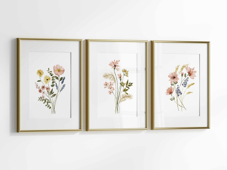 May include: Three framed floral art prints. Each print features a watercolor bouquet of flowers in shades of pink, yellow, and blue. The frames are gold-colored, and the background is white.
