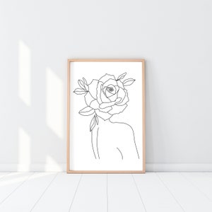 May include: A framed art print featuring a minimalist line drawing of a person with a rose for a head. The artwork is in black and white, with a simple, elegant style. The frame is a light wood color, and the background is white.