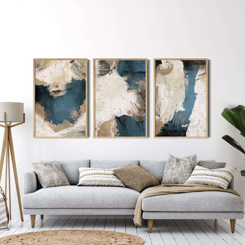 May include: Three abstract art prints with a blue, white, and brown color scheme. The prints are framed in a light wood frame and are hanging on a white wall.