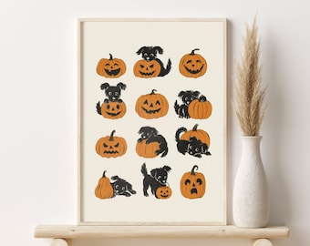 May include: A framed print featuring a repeating pattern of black puppies interacting with orange jack-o'-lanterns. The pumpkins have various carved faces. The print is displayed on a wooden shelf with a white vase and decorative grass.