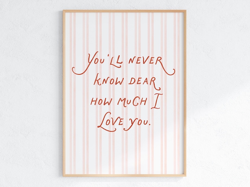 May include: A framed art print with a light wood frame. The background features vertical pink and white stripes. The text in the center reads, "You'll never know dear how much I love you," in a handwritten style, red font.
