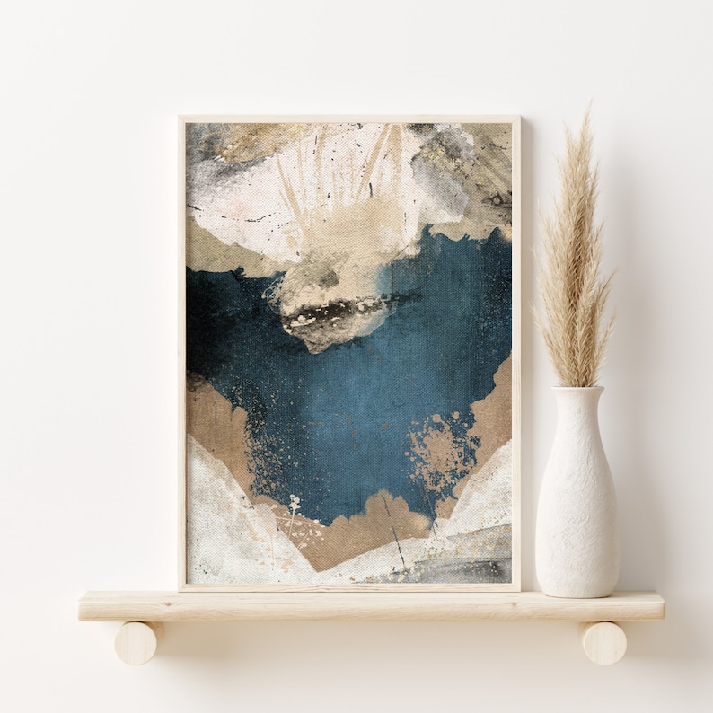 May include: Abstract art print in a white frame with a blue, beige, and white color scheme. The print features a textured background with splattered paint.