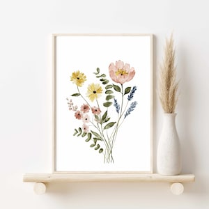 May include: Watercolor floral print featuring a bouquet of flowers in shades of yellow, pink, and blue. The artwork is framed in a light wood frame and displayed on a wooden shelf. A vase with dried grass is to the right.