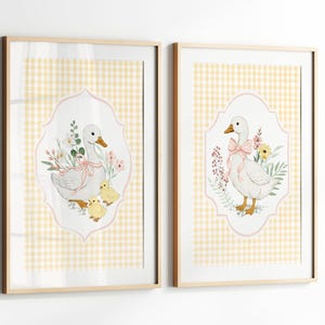 May include: Two framed prints featuring watercolor illustrations of geese. One print shows a goose with two chicks and flowers, the other shows a goose with a pink bow and flowers. Both are set against a yellow gingham background.