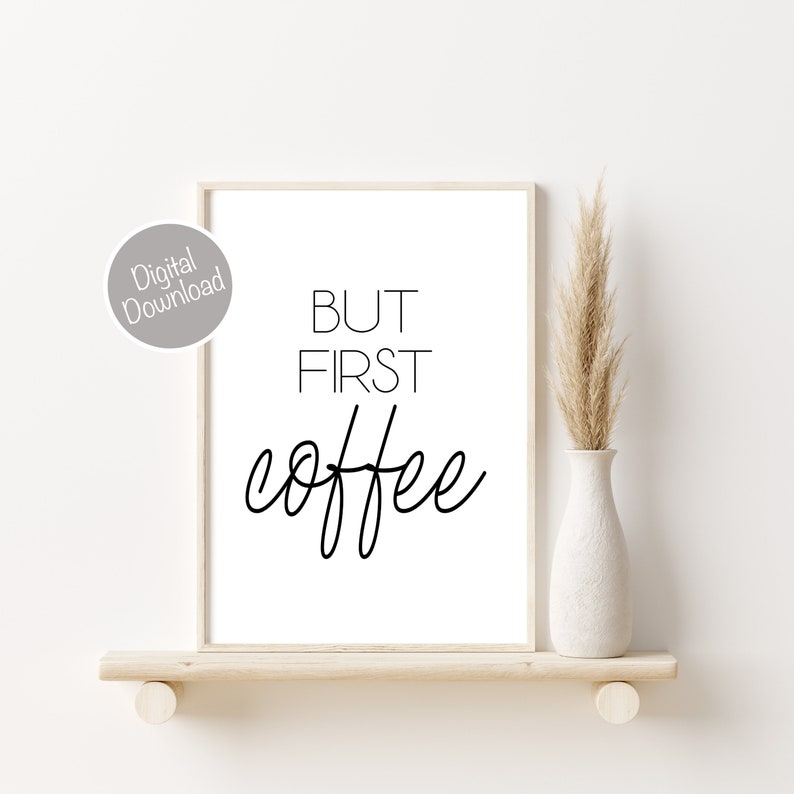 Puede incluir: Una impresi&oacute;n de arte de pared imprimible en blanco y negro con el texto "BUT FIRST COFFEE" en un estilo de caligraf&iacute;a moderno. La impresi&oacute;n est&aacute; enmarcada y se muestra en un estante con un jarr&oacute;n de hierba de la pampa seca.